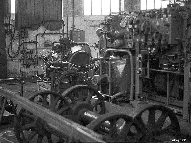 Schwarz-weiß Foto aus einer Werkstatthalle der Bahn. Im Vordergrund Achsen mit Speichenrädern, im Hintergrund wird eine Achse mit Vollrädern in einer großen Maschine abgedreht.
