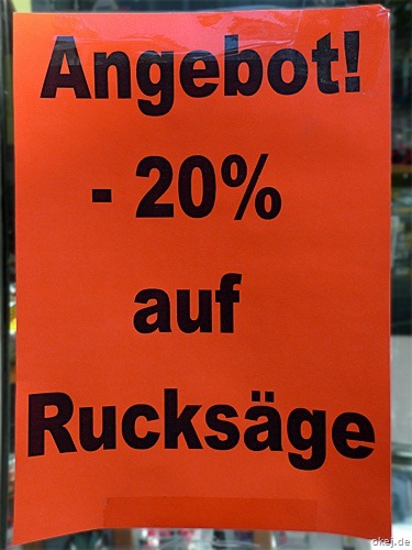 Rotes Plakat in einem Schaufenster mit der Aufschrift "Angebot -20% auf Rucksäge". Also mit Schreibfehler Rucksäge statt Rucksäcke.